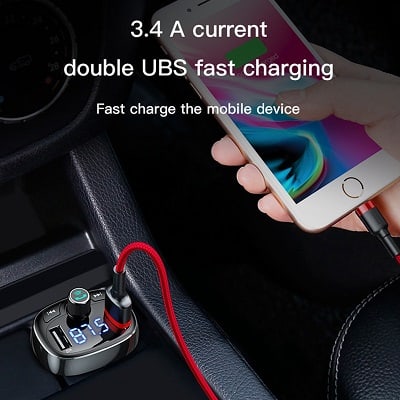 A person using a Baseus Wireless Bluetooth FM Transmitter & MP3 Music Player's dual USB car charger, featuring 3.4 A current double USB fast charging, to charge a smartphone with a red cable connected to it.