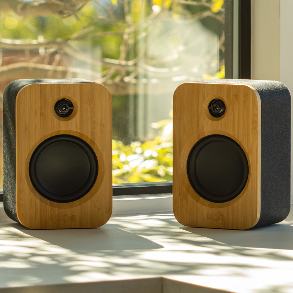 Two MARLEY House of Marley Get Together Duo Bluetooth Wireless Speakers with black grilles sit on a white windowsill, sunlight streaming in and greenery outside, delivering premium sound quality to any room.
