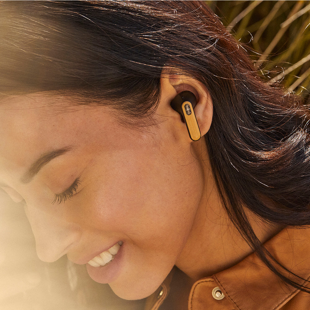 A person wears MARLEY House of Marley Redemption ANC 2 Wireless Earbuds in black, smiling as sunlight highlights their face and hair, enjoying immersive audio.