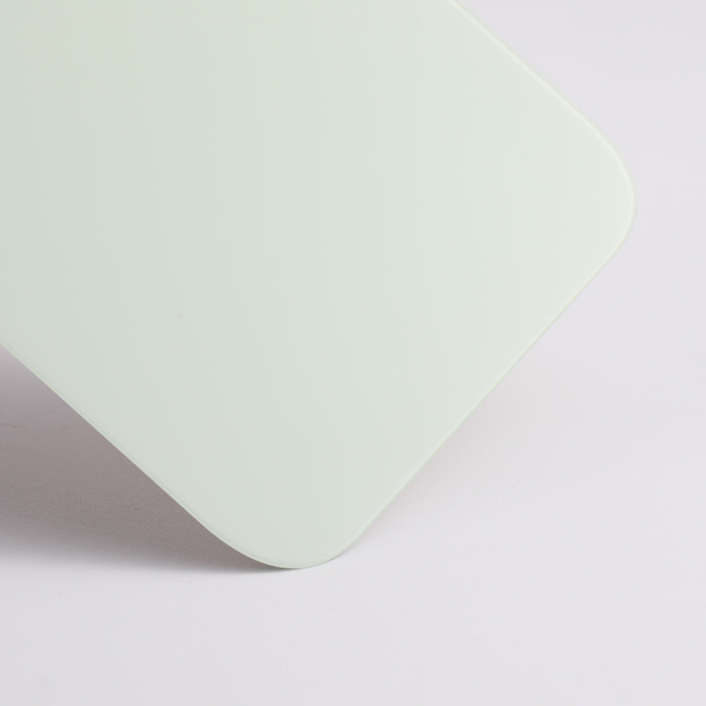 A close-up of the corner of a smooth, rectangular Cirrus-link Back Glass Cover with Big Camera slot for iPhone 12 (AfterMarket), shown in pale green against a white background.