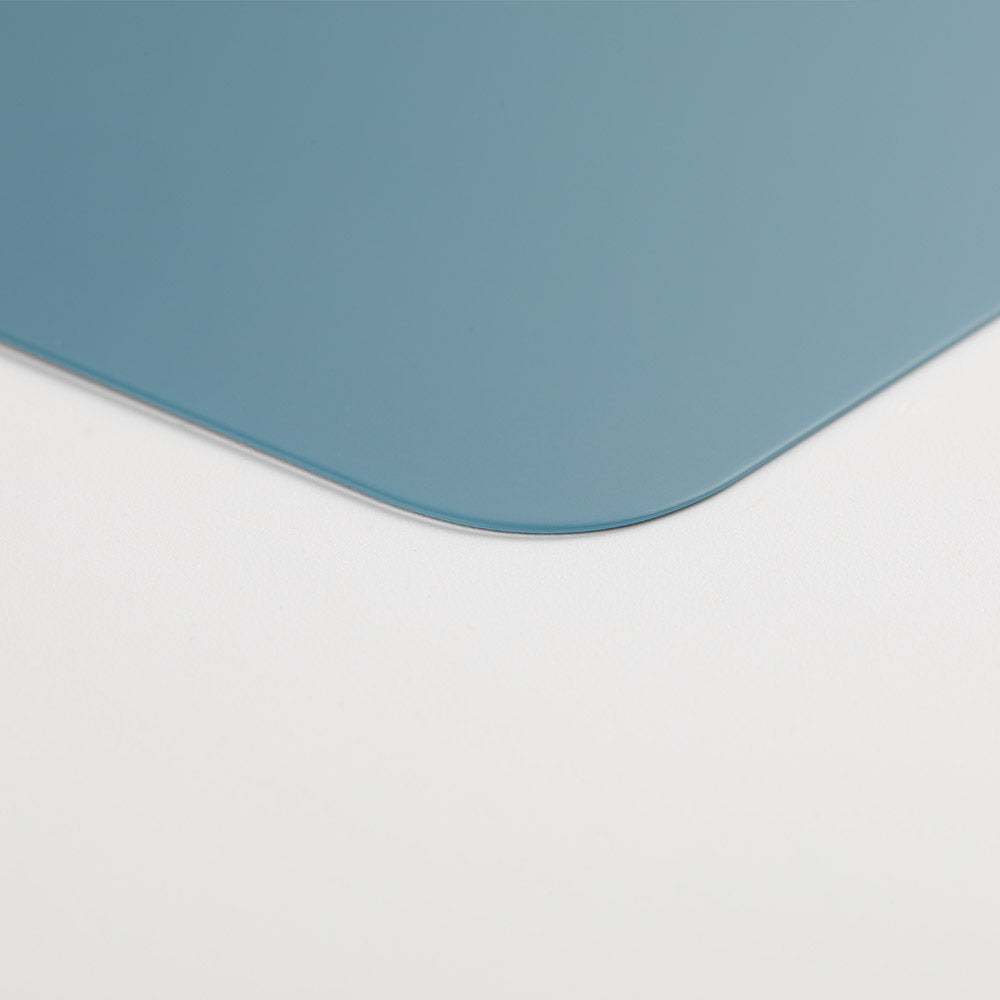 A close-up of the rounded corner of a thin, blue Cirrus-link Back Glass Cover with Big Camera slot for iPhone 12 Pro Max (AfterMarket), shown on a white surface.
