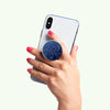 A hand holding a smartphone with a wireless charging compatible blue POPSOCKETS PopGrip Licensed - Enamel Mandalorian featuring a zodiac design.